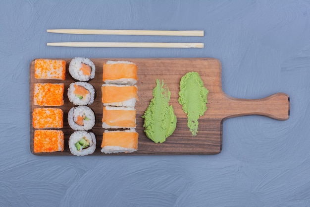 Суши-роллы с соусом васаби на деревянном блюде