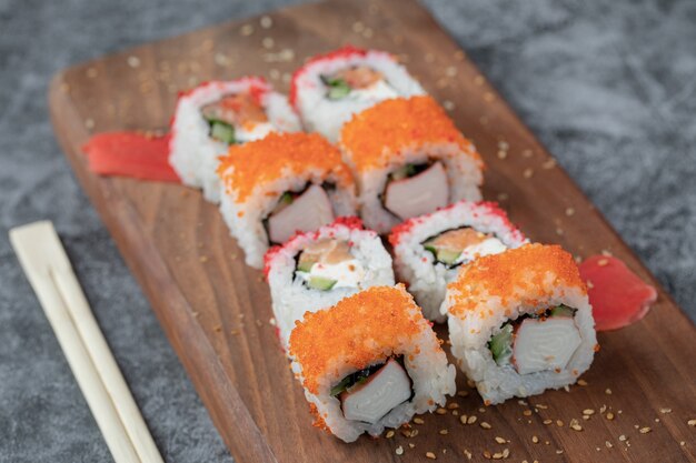 Sushi rolls with yellow and red caviar on a wooden board.