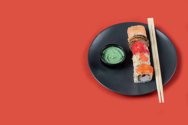 Sushi set with sauces in a black platter on red table.