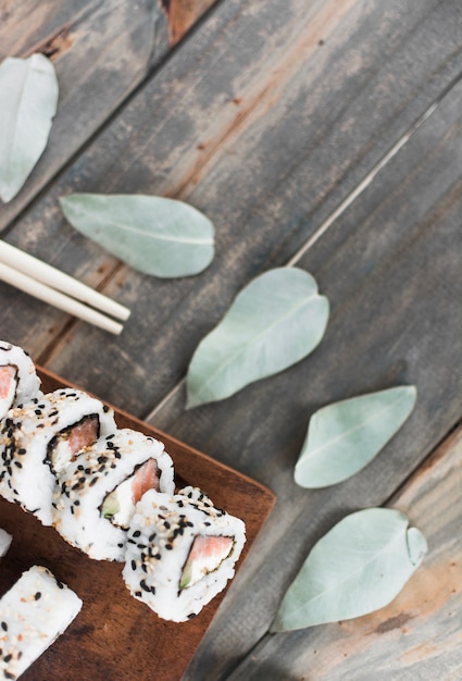 Sushi on wooden tray with leaves and chopsticks on wooden table