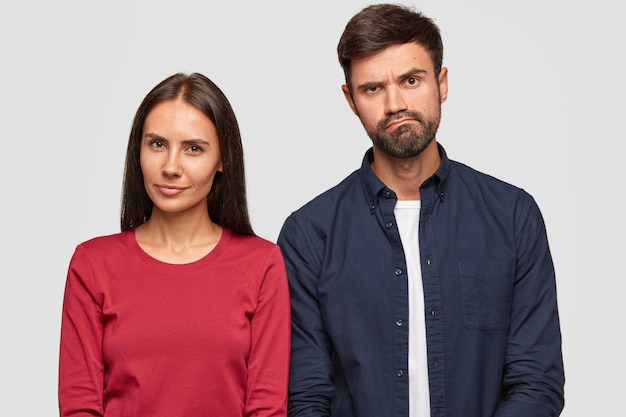 Suspicious beautiful young woman and puzzled unshaven guy stand together, express different emotions