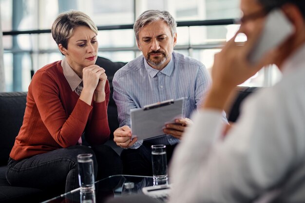 Suspicious couple going through insurance agreement while being on a meeting with their agent