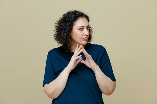 suspicious middleaged woman wearing tshirt keeping hands together looking at camera isolated on olive green background