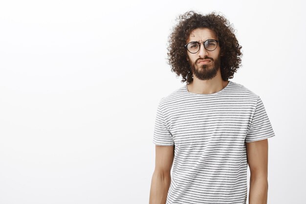 Suspicious thoughtful attractive hispanic guy in trendy glasses, lifting eyebrow in doubt and staring