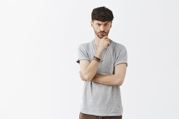 Suspicious and thoughtful handsome guy posing against the white wall