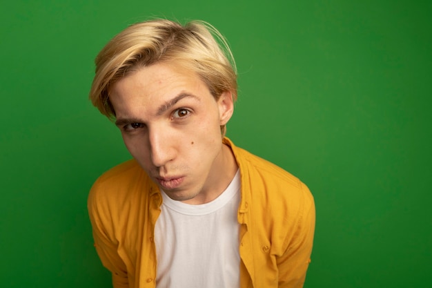 Free photo suspicious young blonde guy wearing yellow t-shirt isolated on green with copy space