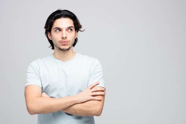 suspicious young handsome man standing with crossed arms looking at side isolated on white background with copy space