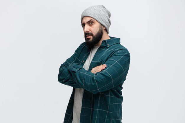 Suspicious young man wearing winter hat standing in profile view with arms crossed looking at camera isolated on white background