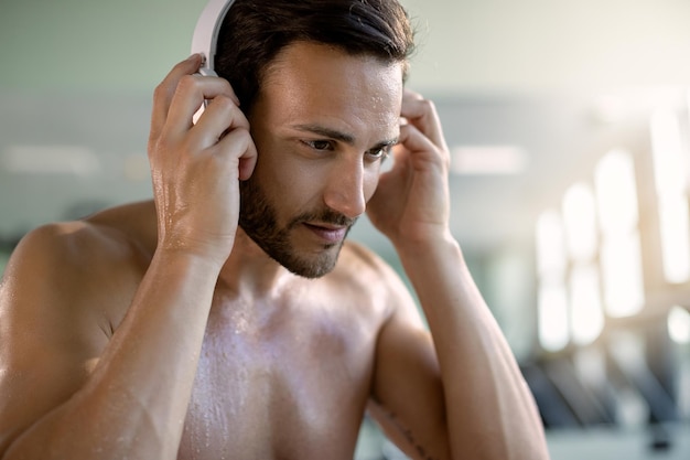 Sweaty athlete listening music over headphones in health club