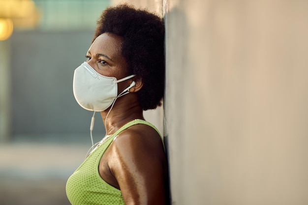 Free photo sweaty black athletic woman with face mask leaning on a wall outdoors