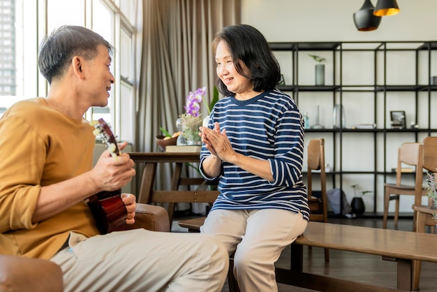 甘いアジアのシニアカップルがアコースティックウクレレ楽器を歌う幸せな笑顔おじいさんが楽しんで、引退生活を楽しんでいますライフスタイルパーティー幸せなライフスタイル