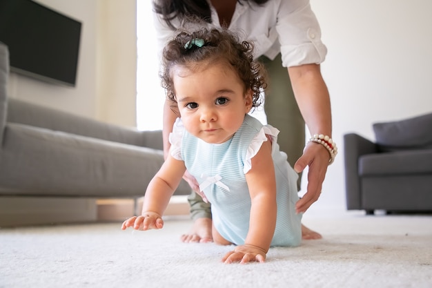 Free photo sweet baby crawling on floor at home, hands of mom going to take child in arms. parenthood and childhood concept