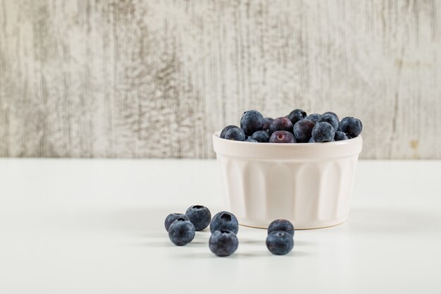 Sweet blueberries in a white bowl side view on a grunge and white background