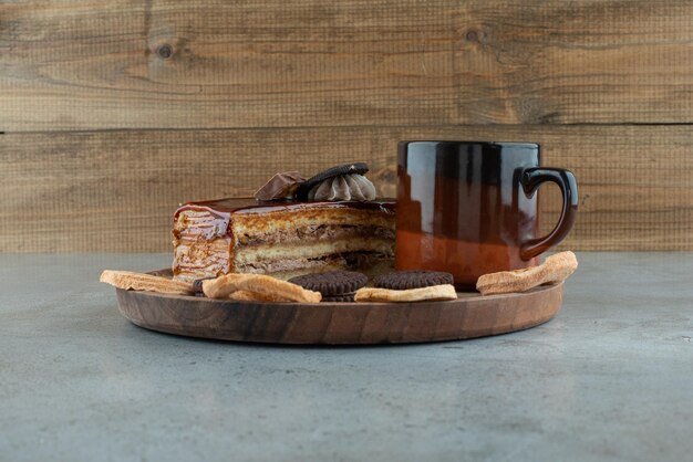 Sweet cake, dried fruits and cup of coffee on wooden plate.