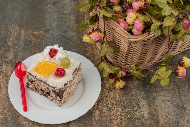 Sweet cake with basket of roses on marble surface