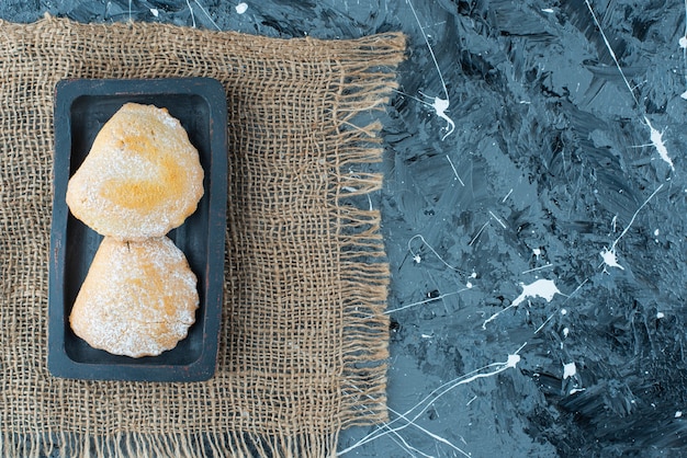 Бесплатное фото Сладкие пирожные на деревянной тарелке на текстуре, на синем столе.