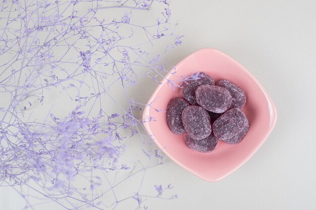 Sweet candies in bowl on beige surface