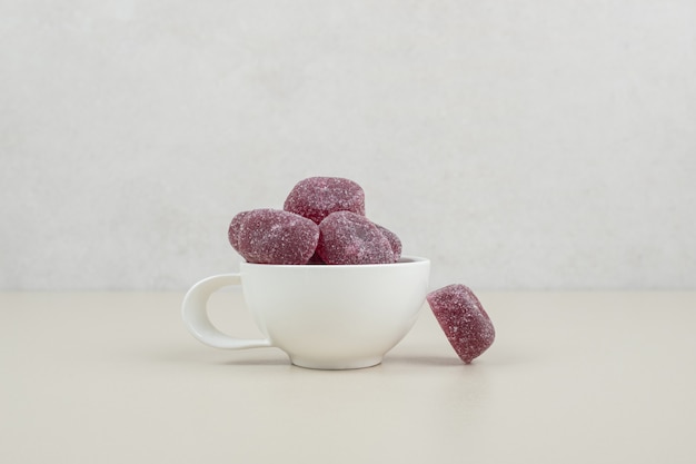 Sweet candies in white mug on beige surface