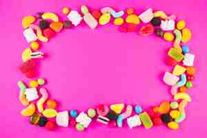 Free photo sweet candies with various shapes forming frame on pink surface