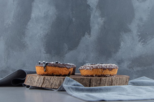 Sweet chocolate donuts on wood piece on stone surface