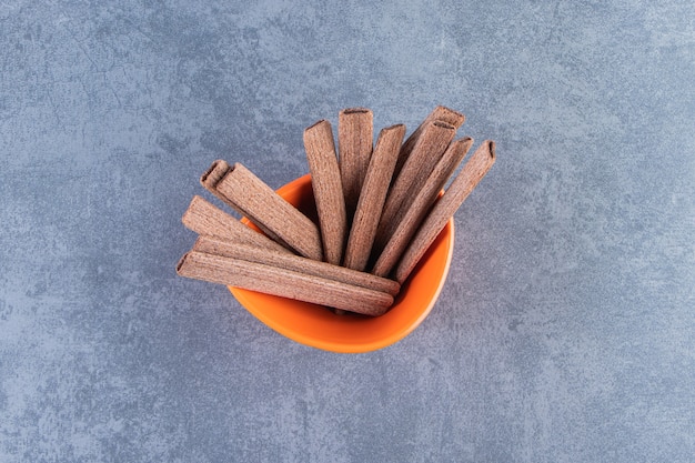 Sweet chocolate wafer roll in a bowl, on the marble background.