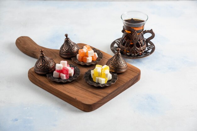 Sweet colorful candies on wooden board beside of Fresh hot tea