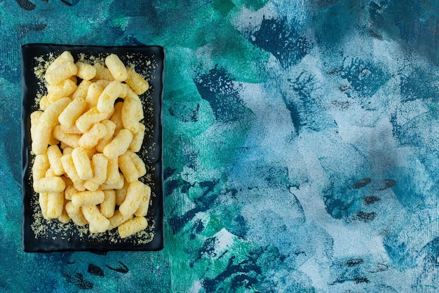 Bastoncini di mais dolce su un piatto, sul tavolo blu.