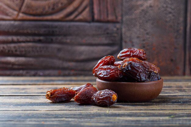 Sweet dates in a clay plate on stone tile and wooden background