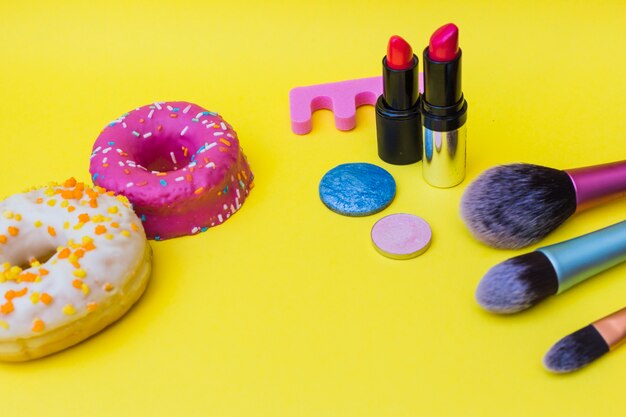 Sweet donut; toe divider; lipstick; makeup brush and eye shadow on yellow background