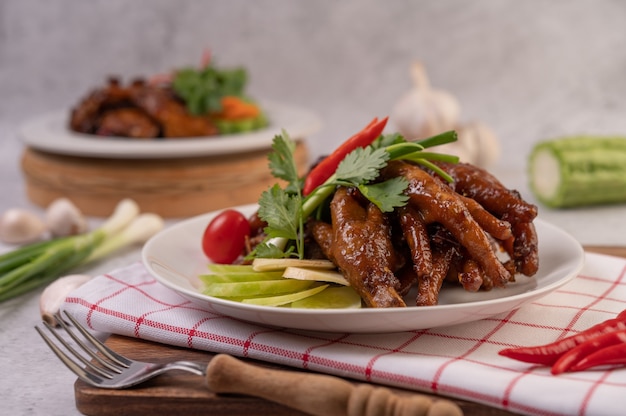 Sweet fried chicken feet in a white plate with coriander, chili, cucumber, and tomato.