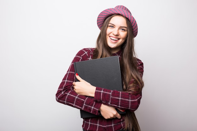 Sweet friendly young student girl holding colorful exercise books isolated on white wall