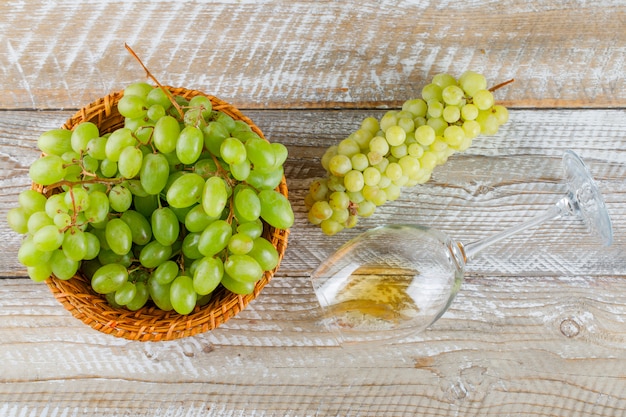 Sweet grapes in a wicker basket with drink flat lay on a wooden background