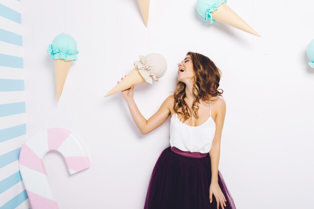 Sweet happy moments of attractive fashionable young woman in tulle skirt having fun with huge cone ice cream. Dreaming,  delicious, enjoying, happiness, smiling.