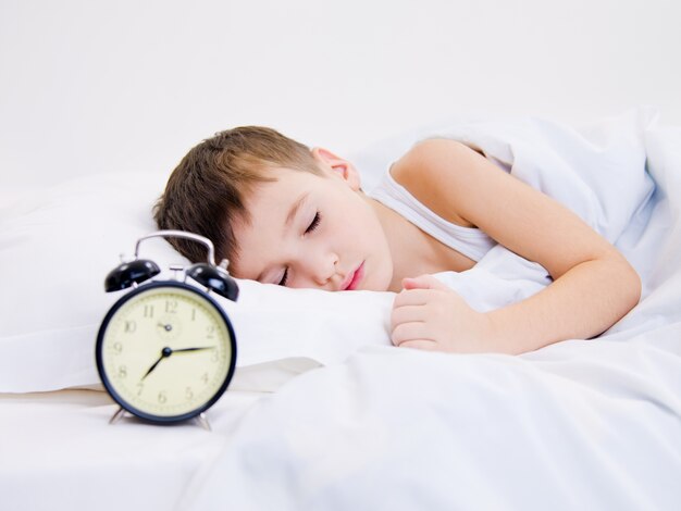 Sweet kid sleeping with alarm clock near his head