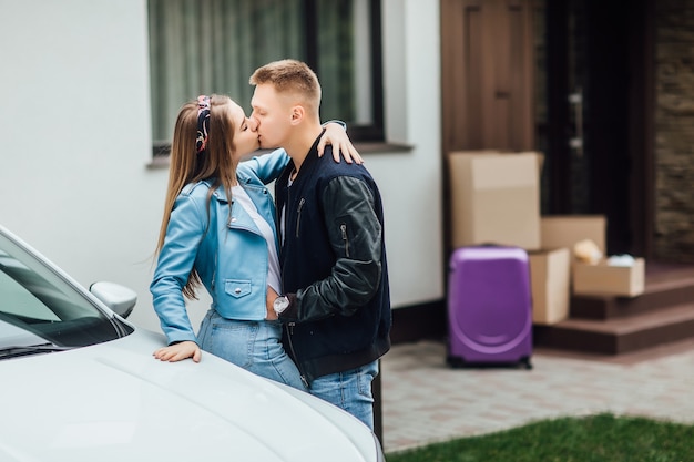 Сладкий поцелуй. Счастливая пара стоит возле новой машины и дома с картонными коробками.