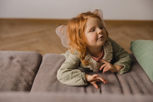 Dolce bambina caucasica con capelli rossi giace sul divano al mattino concetto di infanzia