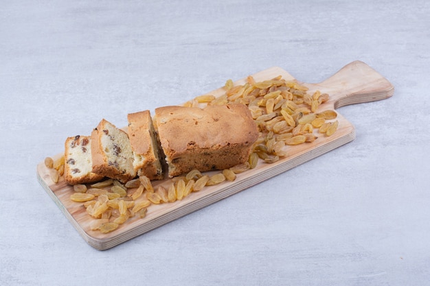 Sweet loaf with bunch of raisins on wooden board.