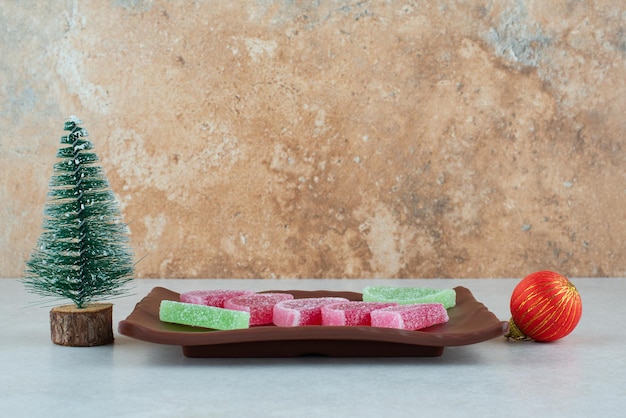 Marmellata dolce con palla di natale e albero sul piatto scuro.