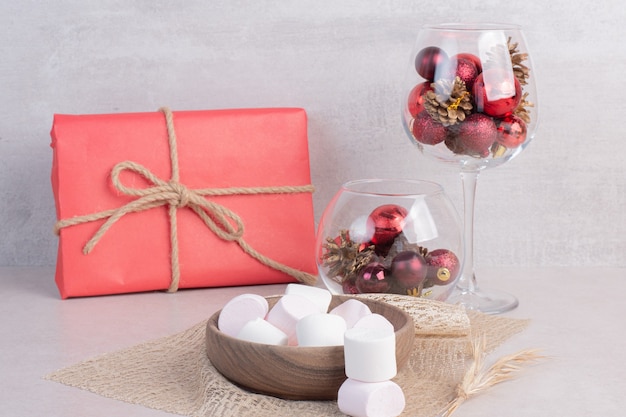 Sweet marshmallows on wooden plate with glass of Christmas red balls