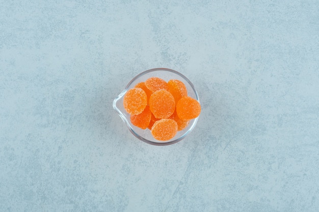 Sweet orange jelly candies with sugar in a glass plate on a white surface