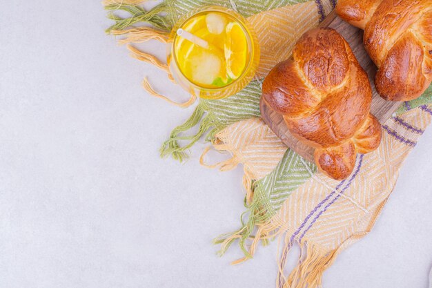 Sweet pastry buns on wooden platter with a glass of lemonade.