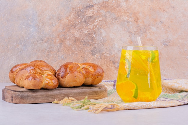 Sweet pastry buns on wooden platter with a glass of lemonade.