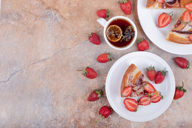 Sweet pie with strawberry in a white plate with a cup of tea