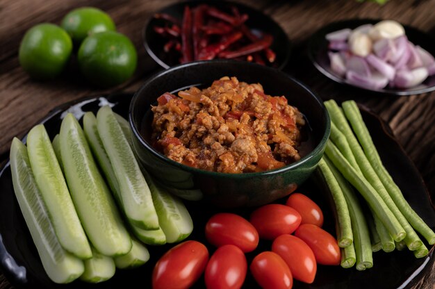 오이, 긴 콩, 토마토 및 반찬이 들어있는 검은 그릇에 달콤한 돼지 고기