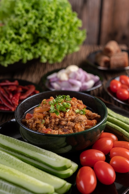 Sweet pork in a black bowl, complete with cucumbers, long beans, tomatoes, and side dishes