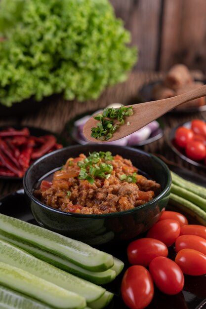 Sweet pork in a black bowl, complete with cucumbers, long beans, tomatoes, and side dishes