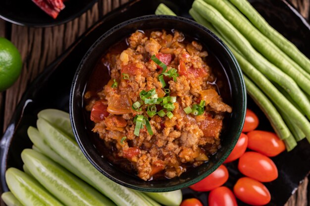 오이, 긴 콩, 토마토 및 반찬이 들어있는 검은 그릇에 달콤한 돼지 고기