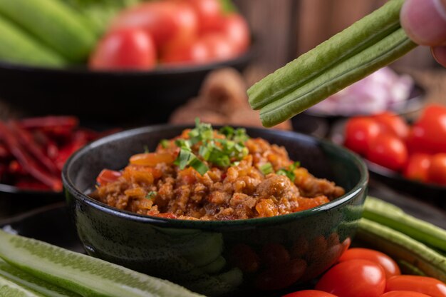 오이, 긴 콩, 토마토 및 반찬이 들어있는 검은 그릇에 달콤한 돼지 고기