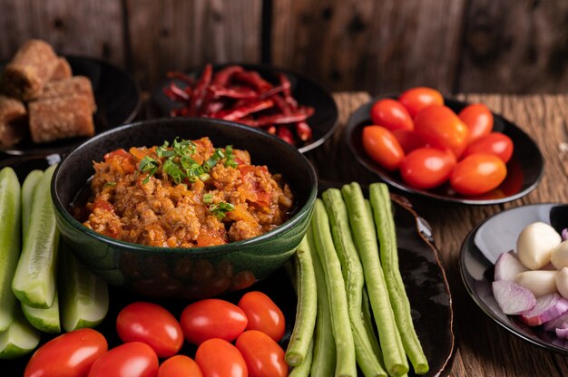 Сладкая свинина в черной миске с огурцами, длинной фасолью, помидорами и гарнирами