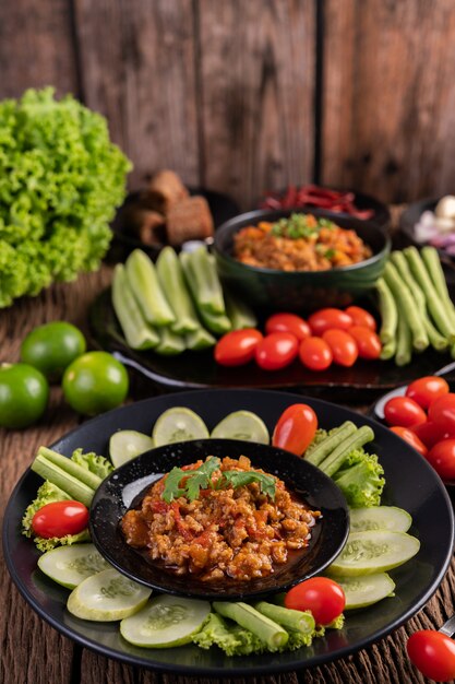 Sweet pork in a black bowl, complete with cucumbers, long beans, tomatoes, and side dishes